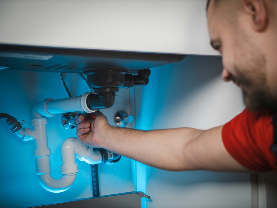 Un plombier serre un raccord sous un lavabo